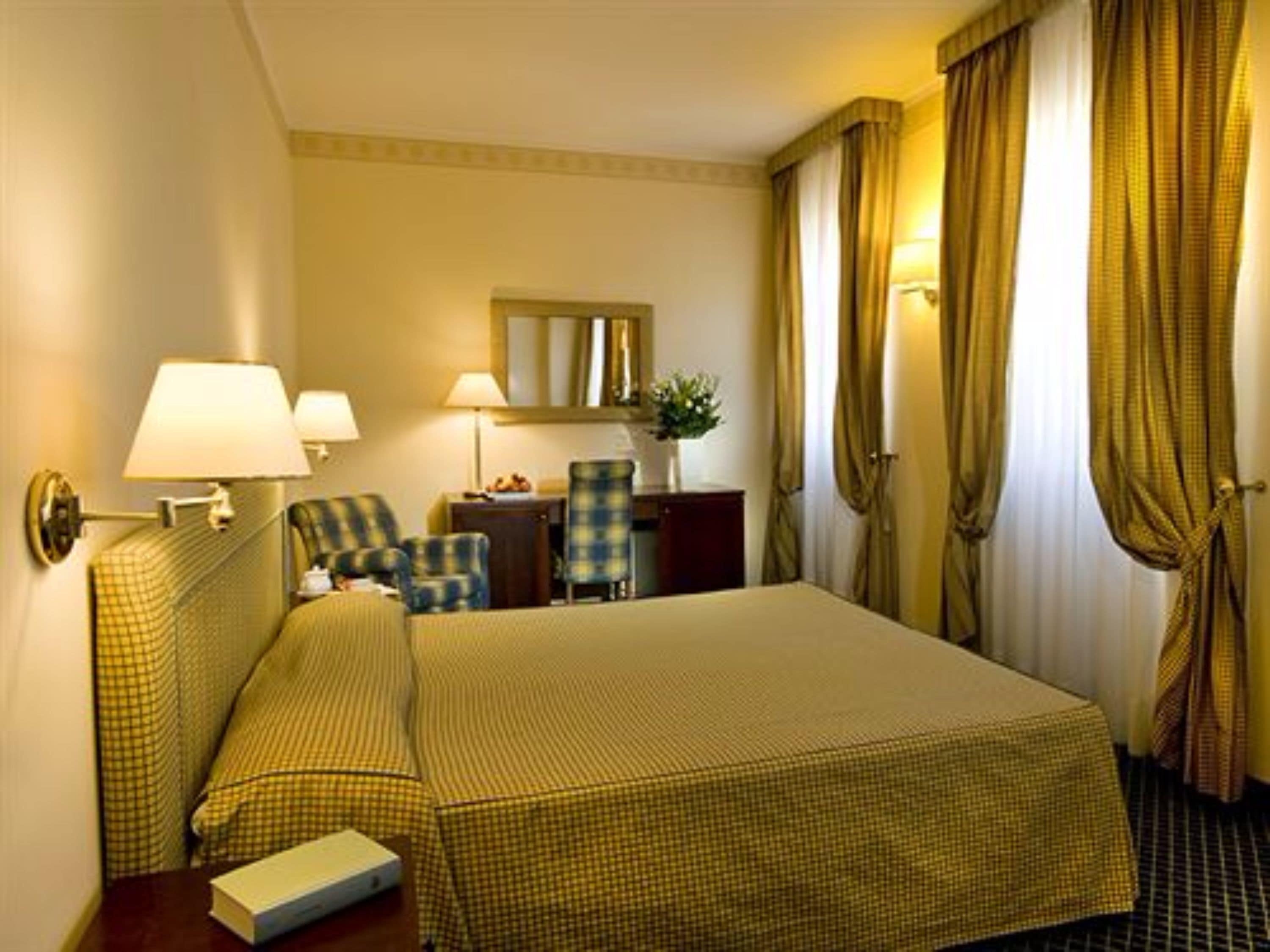 Camera d'albergo con un letto grande, due poltrone, una scrivania e uno specchio.