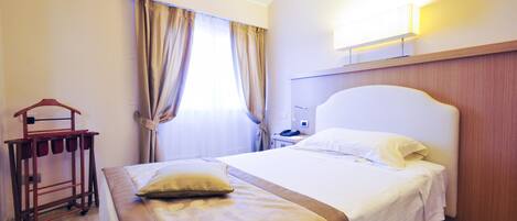 A hotel room with a large bed, a wooden headboard, a bedside table with a lamp, and a wardrobe.