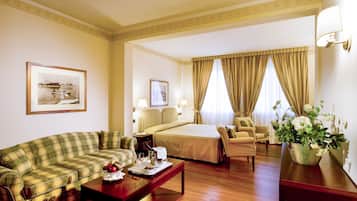 A hotel room with a bed, a sofa, a chair, a dining table, and a vase of flowers.