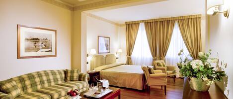 Una habitación de hotel con cama, sofá, sillón, mesa de comedor y un florero con flores.