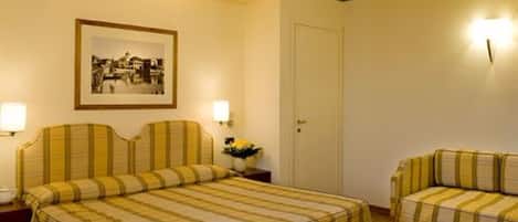 Habitación de hotel con cama, mesita de noche, lámpara, un cuadro enmarcado en la pared y una puerta.
