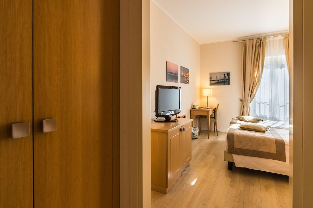 Ein Hotelzimmer mit Bett, Schreibtisch mit Computer, Fernseher und einem Fenster mit Vorhängen.