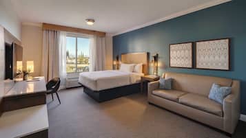 A hotel room with a bed, a sofa, a desk, and a large window with curtains.