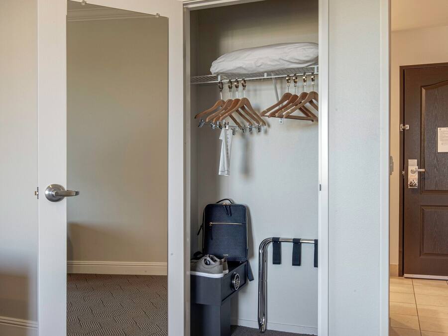 A hotel room with a walk-in closet, a suitcase, and a coat rack.