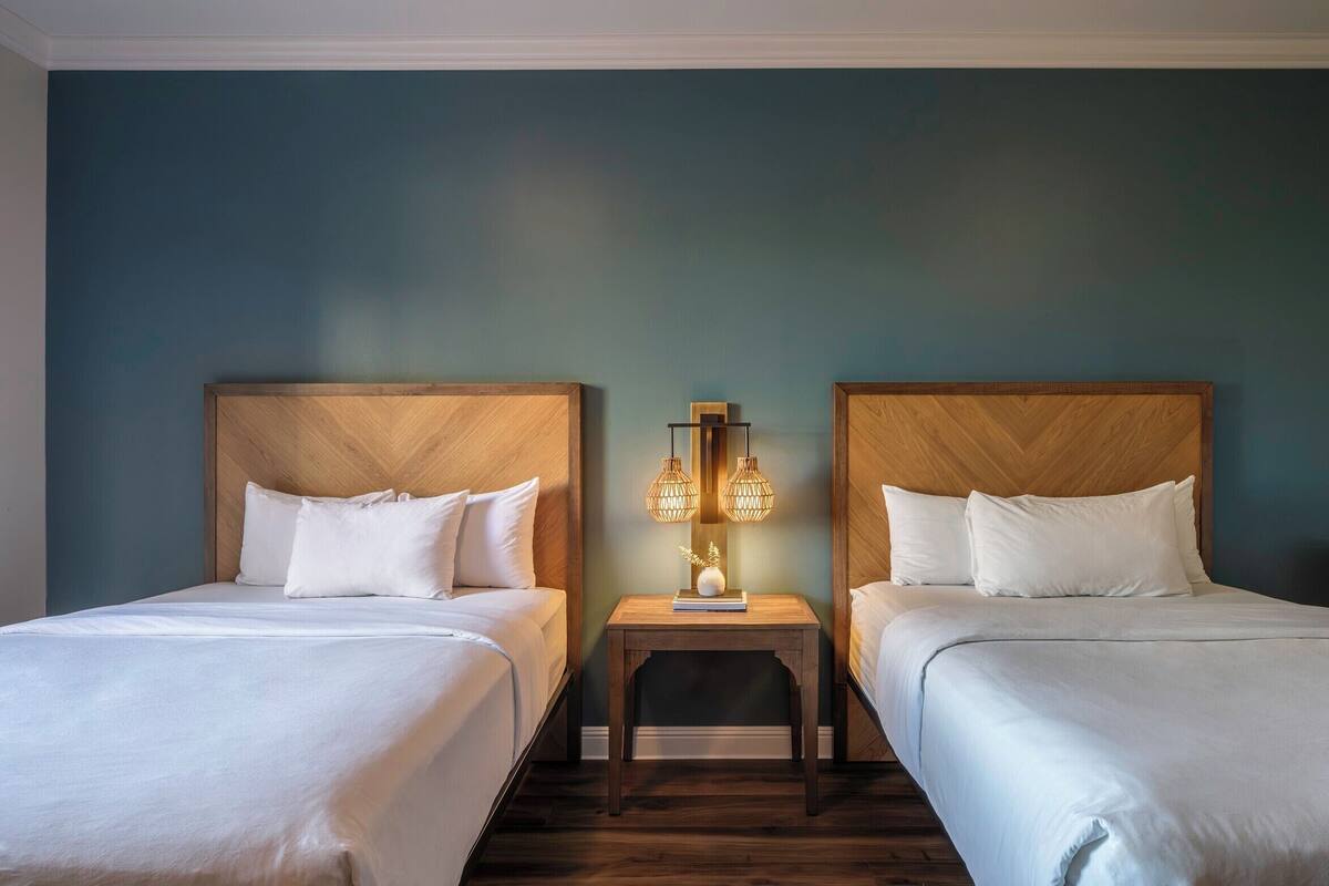 Ein Hotelzimmer mit zwei Betten, Holz-Kopfteilen, einem Nachttisch mit Lampe und einer blauen Wand.