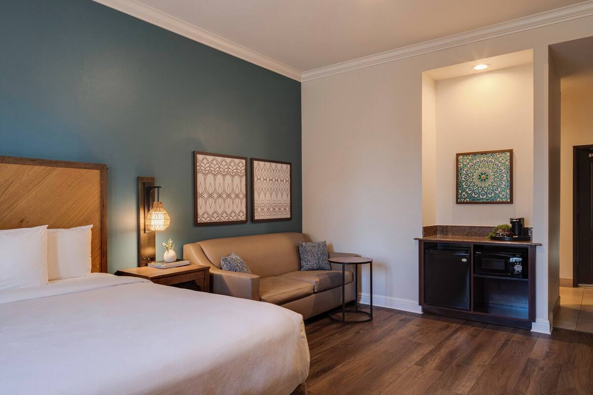 Ein Hotelzimmer mit Bett, einer Couch, einem kleinen Tisch, einer Lampe und einer Küchenzeile.