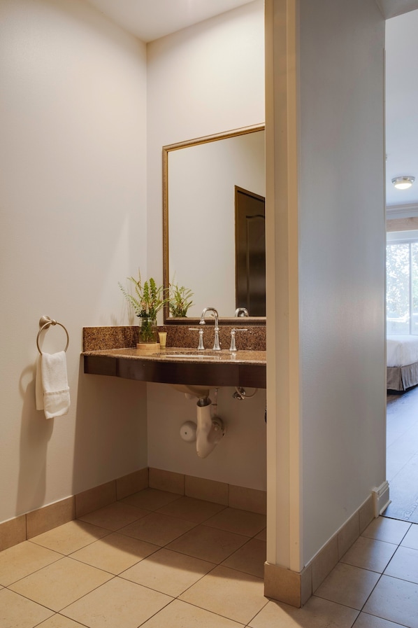 Un baño con lavamanos, espejo, argolla para toallas y una planta en maceta.