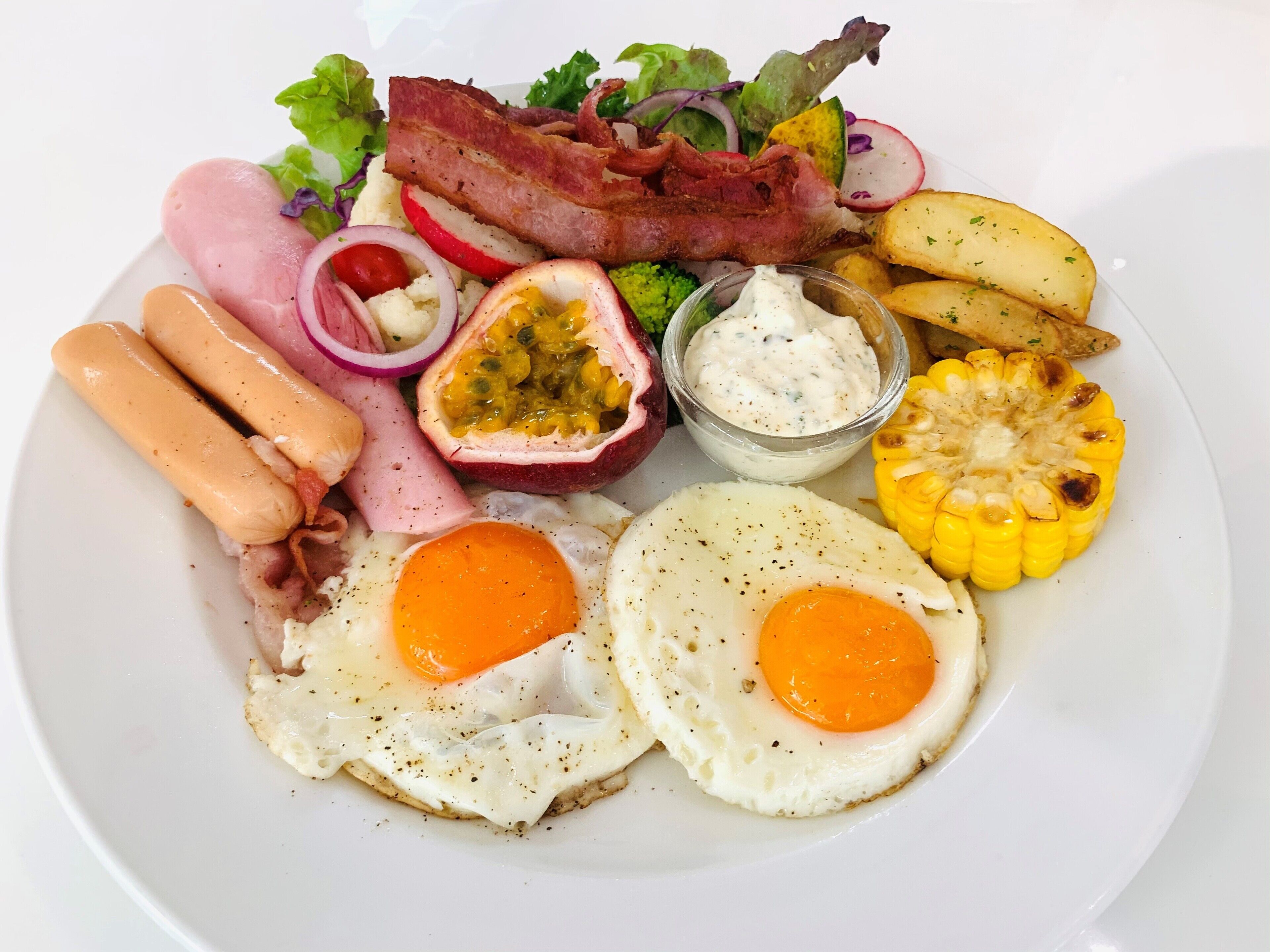Een bord met eieren, spek, worstjes, een salade en verse mais.
