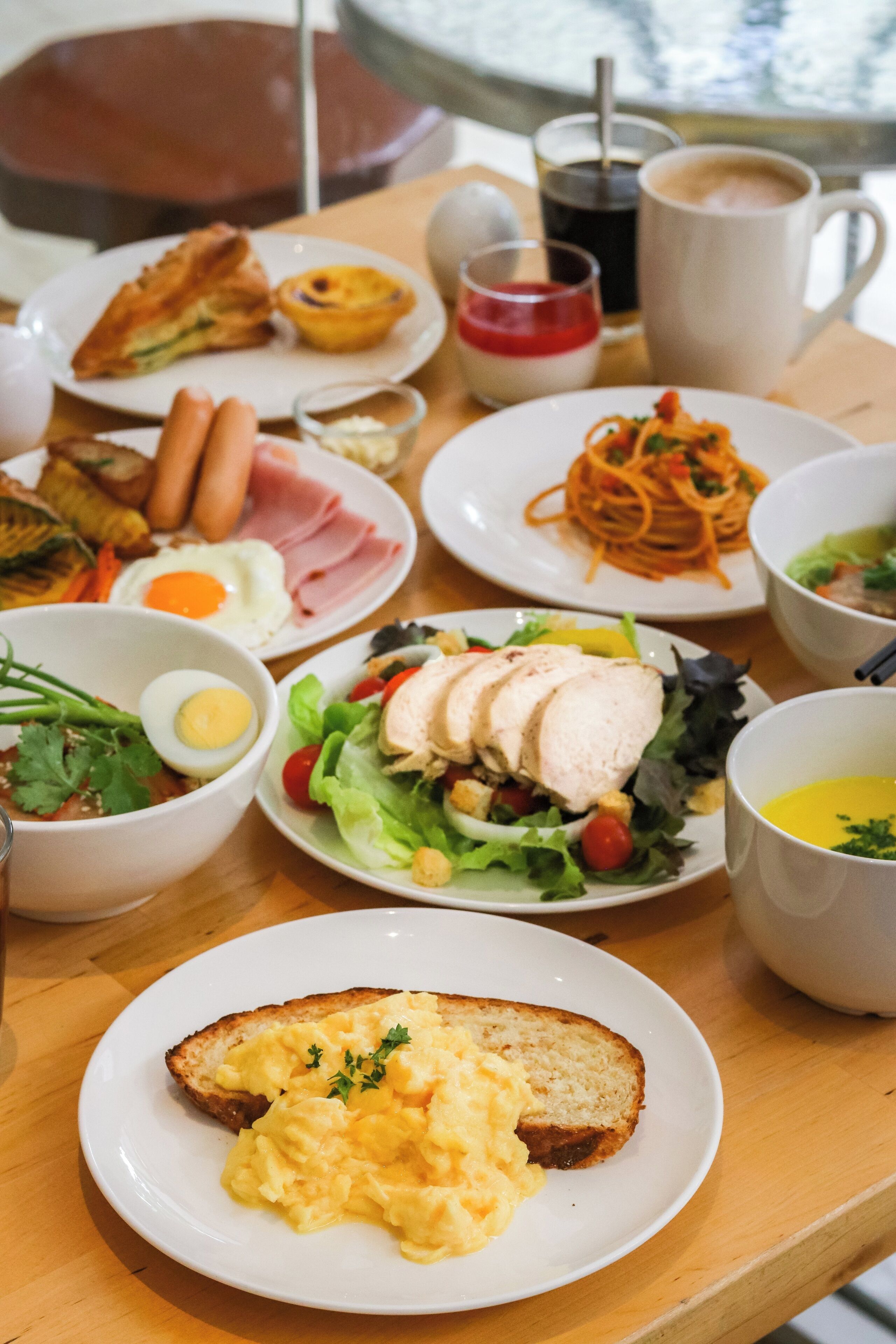 A variety of breakfast dishes on a wooden table, including scrambled eggs, toast, and a salad.
