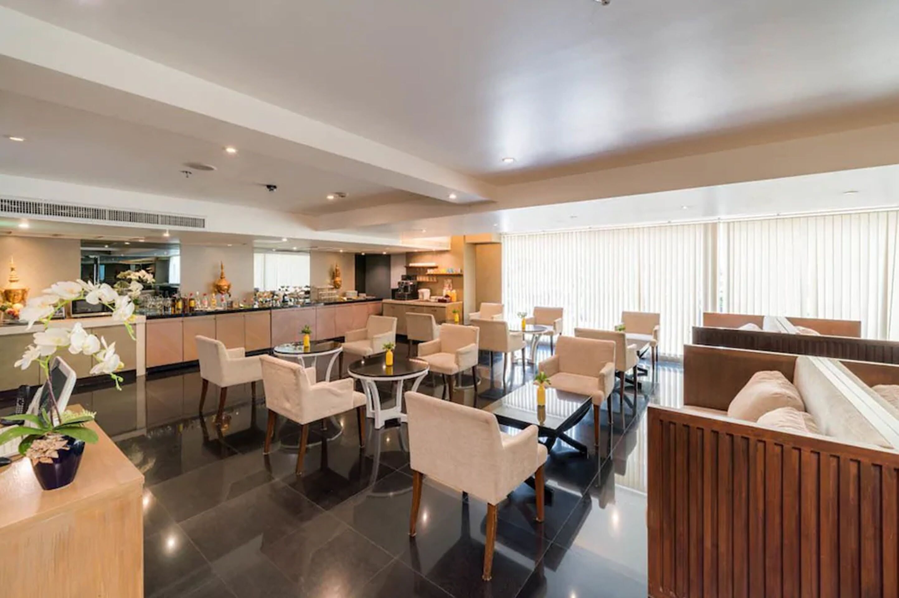 Een moderne hotel lobby met een centraal gelegen eetgedeelte, een keuken op de achtergrond en grote ramen voor natuurlijk licht.