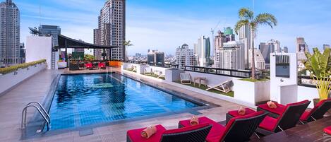 A rooftop pool with a city view, lounge chairs, and a covered seating area.