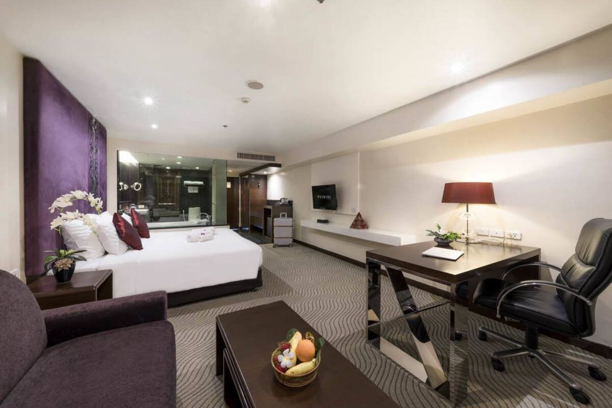 Ein Hotelzimmer mit Bett, Schreibtisch, Stuhl, Couchtisch und Fernseher.