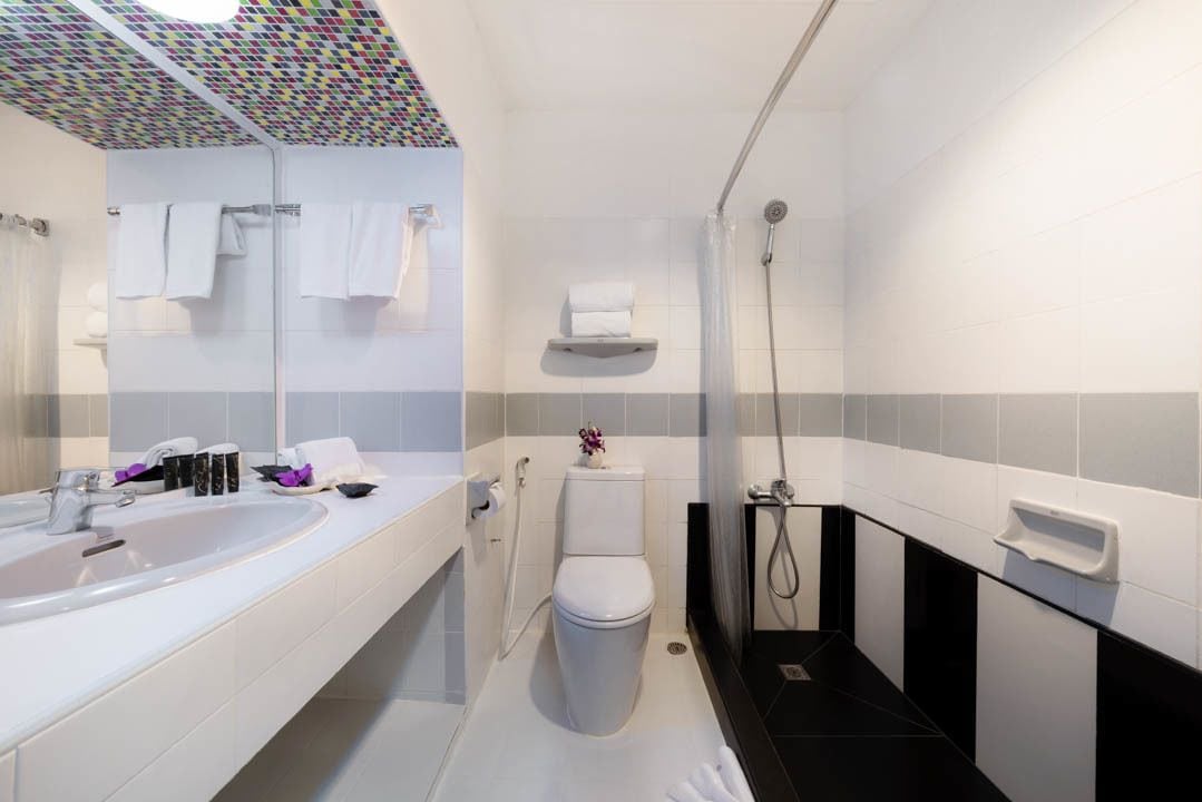 A modern bathroom with a white sink, toilet, and shower. There are towels hanging on a rack and a soap dispenser on the wall.