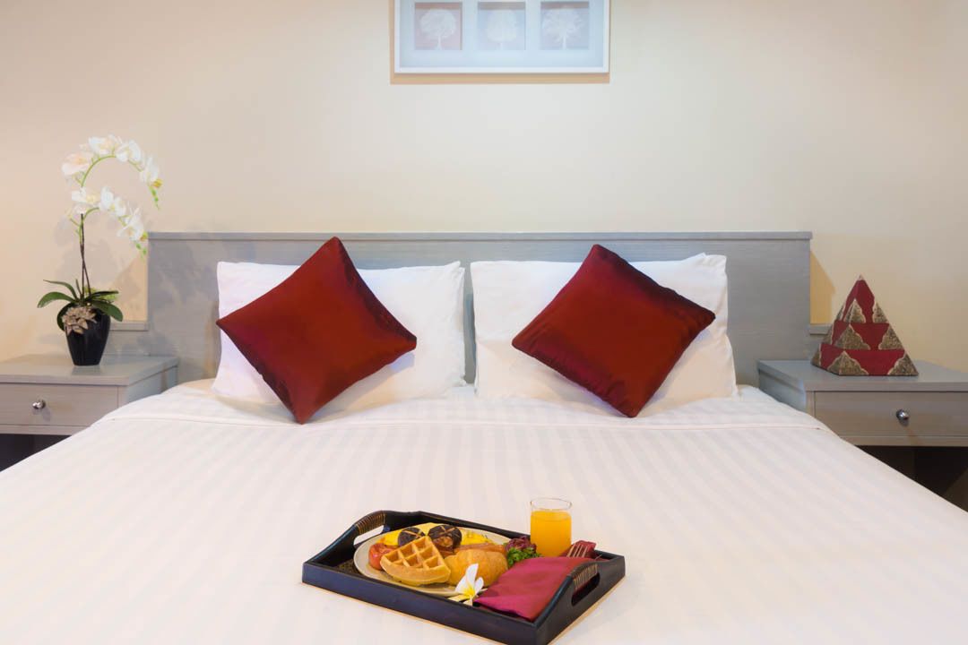 A neatly made bed with two red pillows, a tray with waffles, a glass of orange juice, and a small potted orchid.