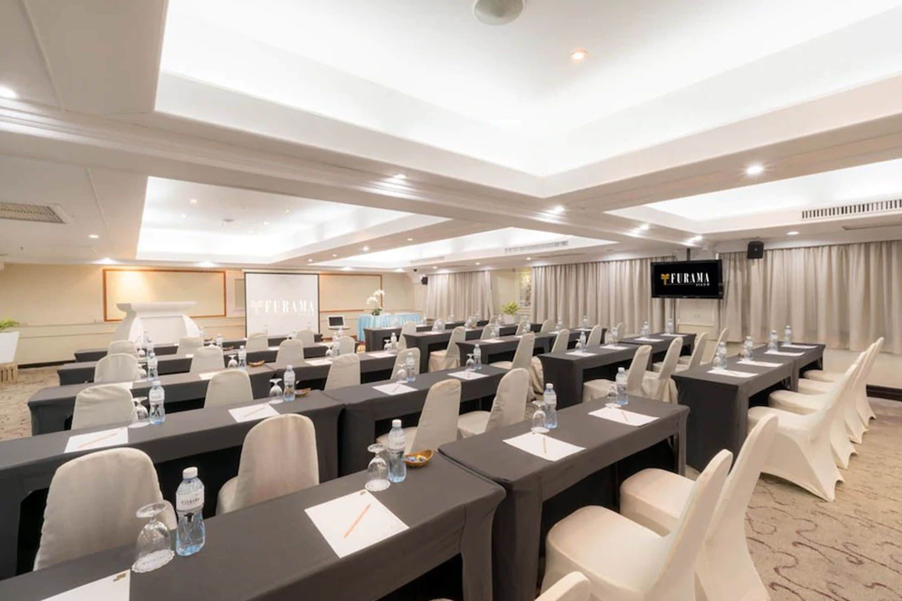 A conference room with multiple tables, chairs, and a large screen.