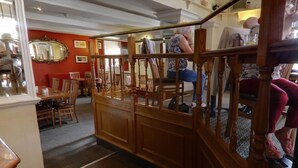 A room with a wooden staircase, a dining area with chairs, and a mirror on the wall. - The Railway Inn (Brixham)