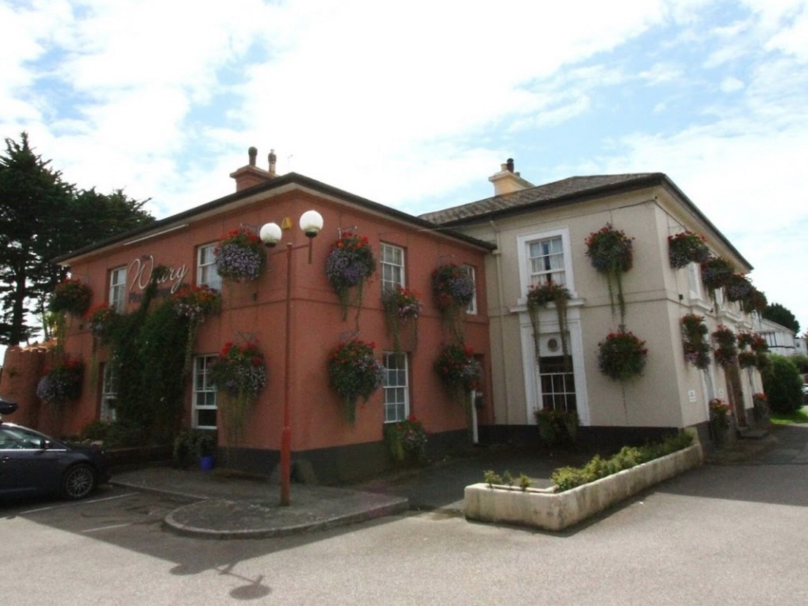 A building with a red facade and a beige section, featuring multiple windows with hanging flower baskets.