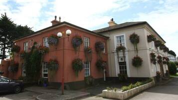 A building with a red facade and a beige section, featuring multiple windows with hanging flower baskets.