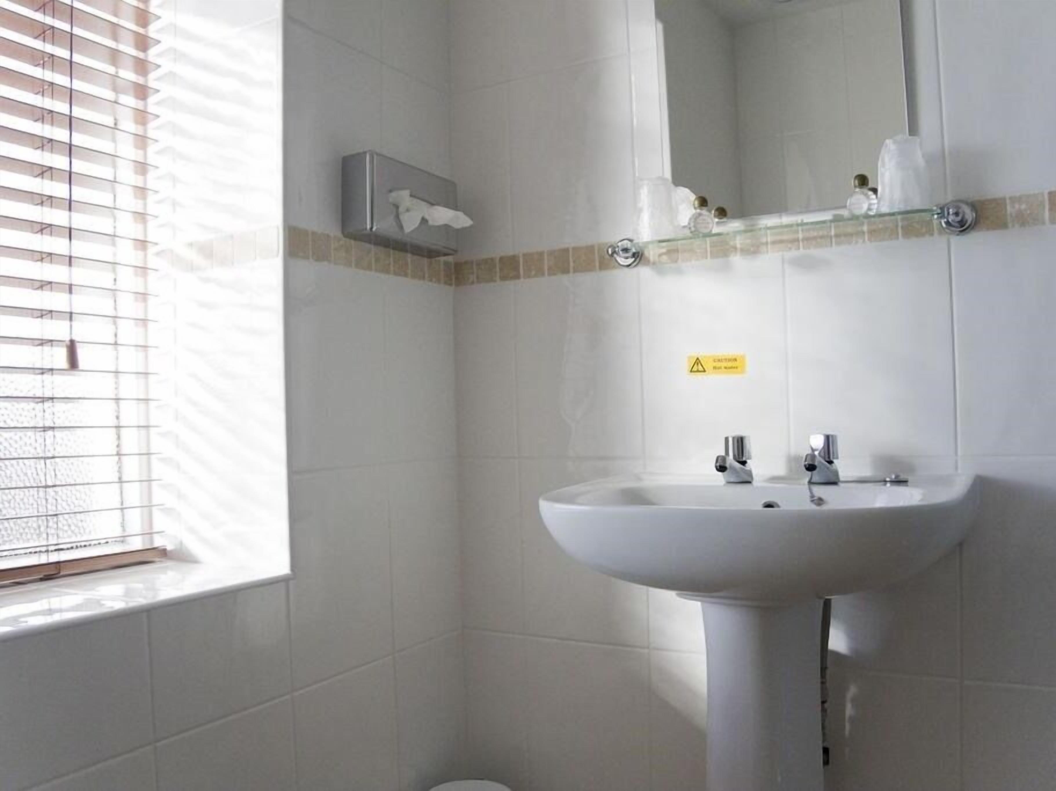 Une salle de bain avec un lavabo blanc, un miroir et une fenêtre avec des stores.