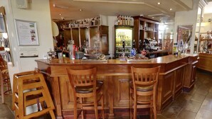 A bar area with wooden chairs, a bar counter, and shelves stocked with bottles. - The Railway Inn (Brixham)