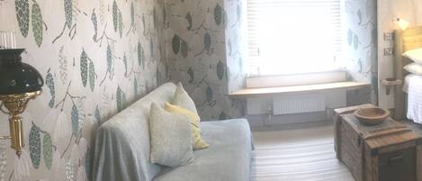 Um quarto acolhedor com um sofá, um baú de madeira, uma luminária e uma janela com persianas.