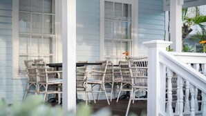 A porch with wicker chairs and a table, white railings, and a window with a view of a palm tree. - Duval Gardens at Southernmost Beach Resort – Adults Only (Key West)