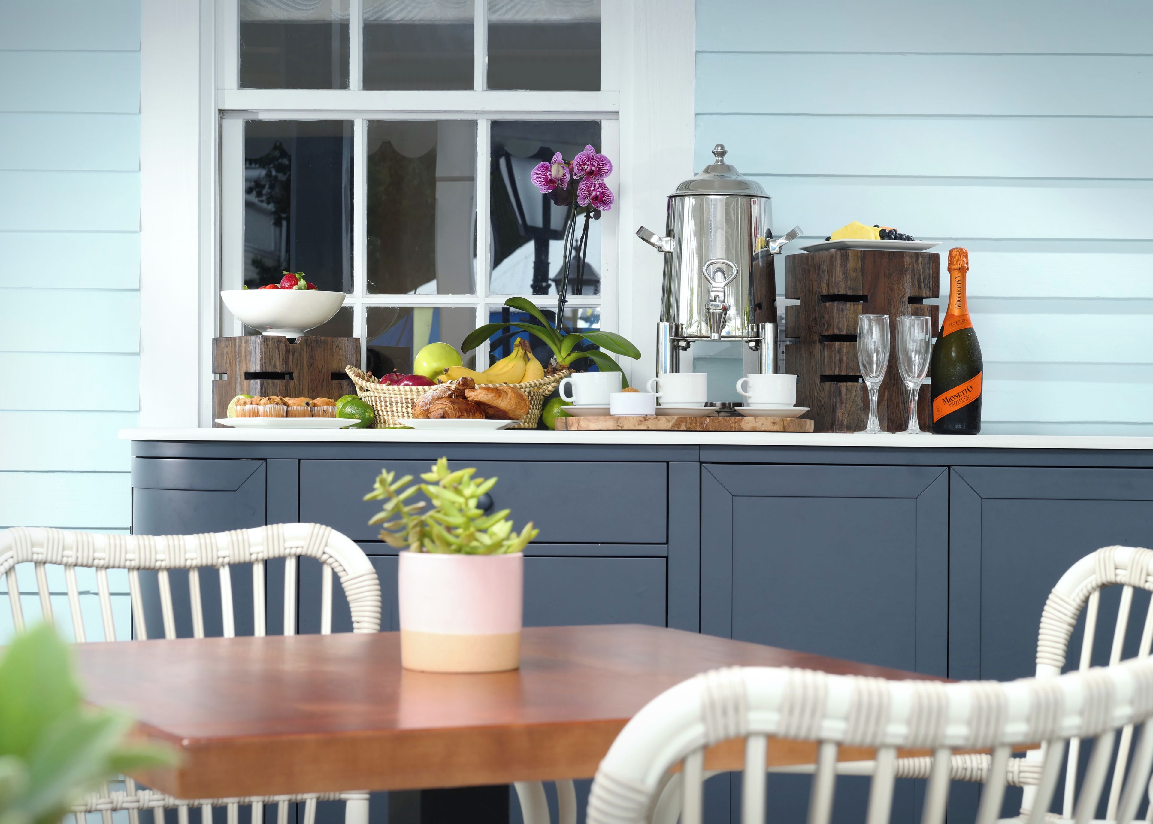 Una encimera de cocina con cafetera, una botella de champán y diversas frutas y pasteles.