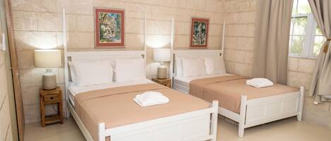 Una habitación con dos camas, cada una con mesita de noche y lámpara, cuadros en la pared y una ventana con cortinas.
