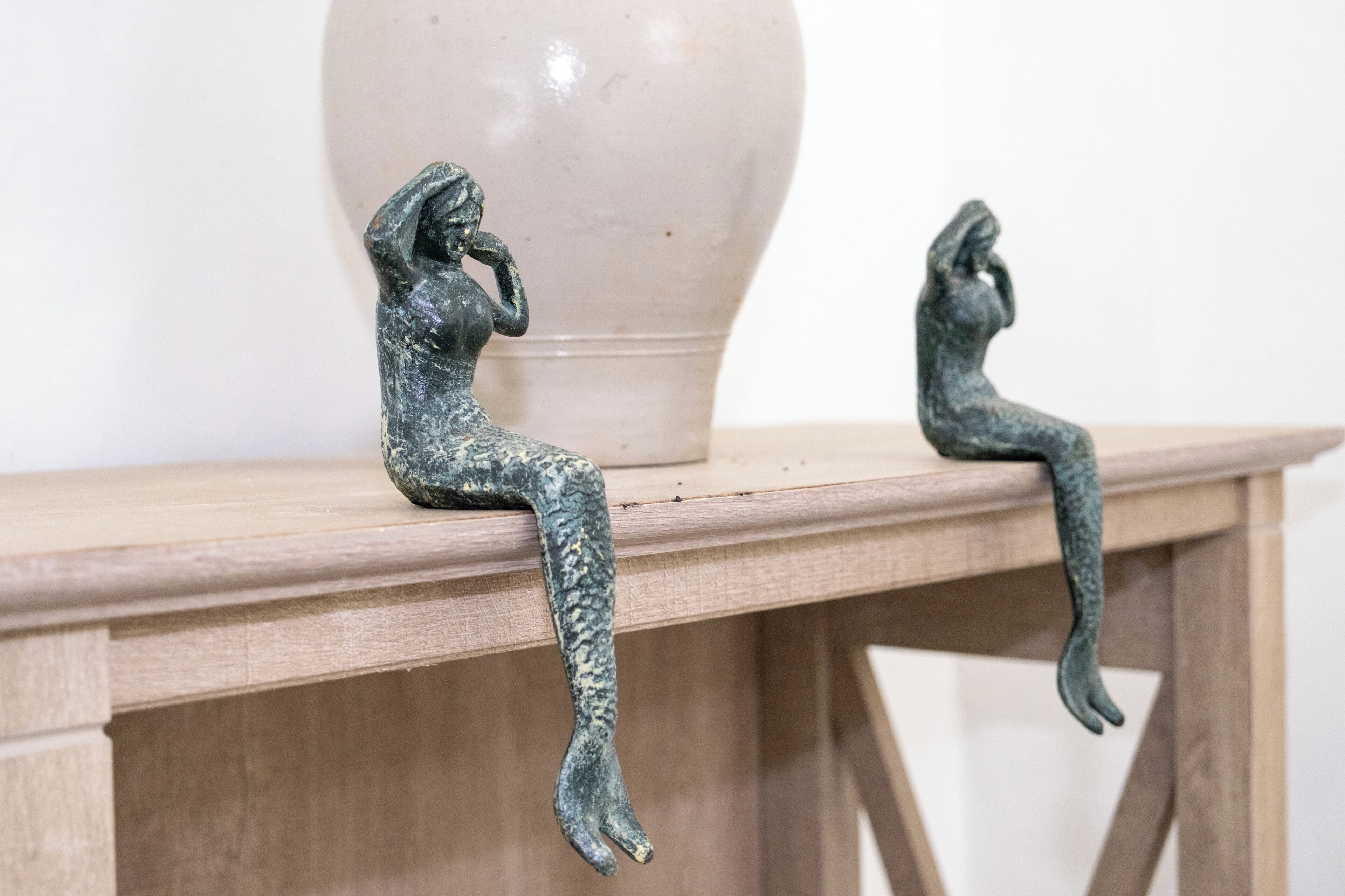 Dos esculturas de bronce sobre una mesa de madera, con un florero al fondo.