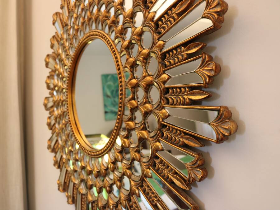Un espejo montado en la pared con un marco ornamentado dorado.