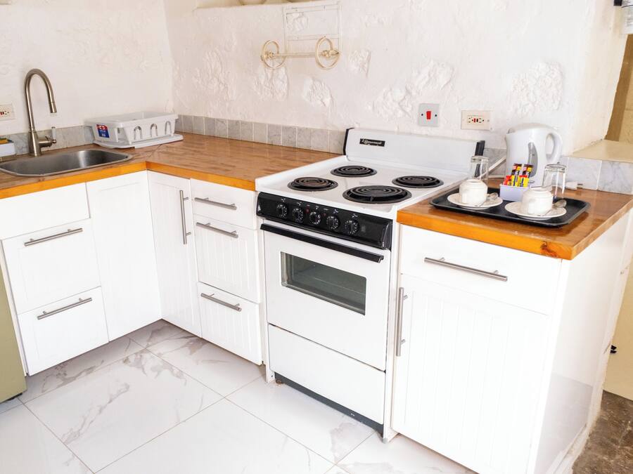 Cocina compacta con armarios blancos, estufa, lavaplatos y cafetera.