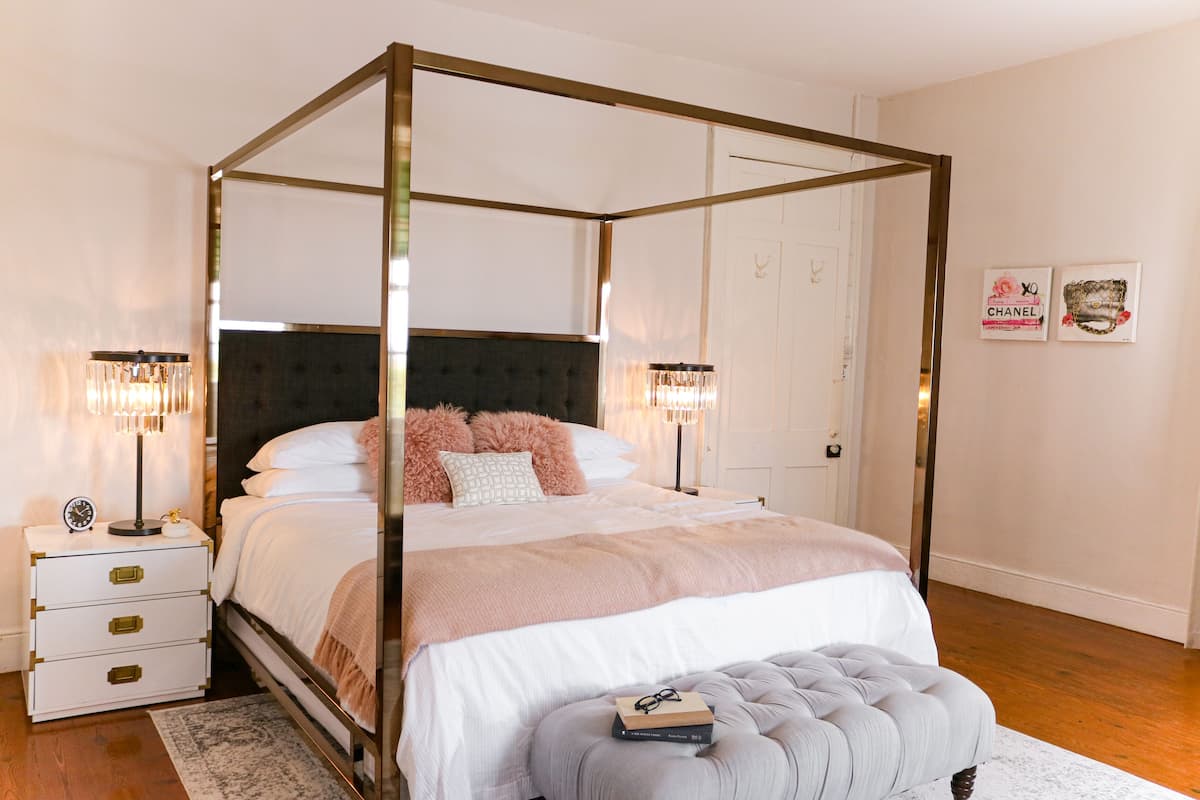 A four-poster bed with a tufted headboard, bedside tables with lamps, and a bedside clock.