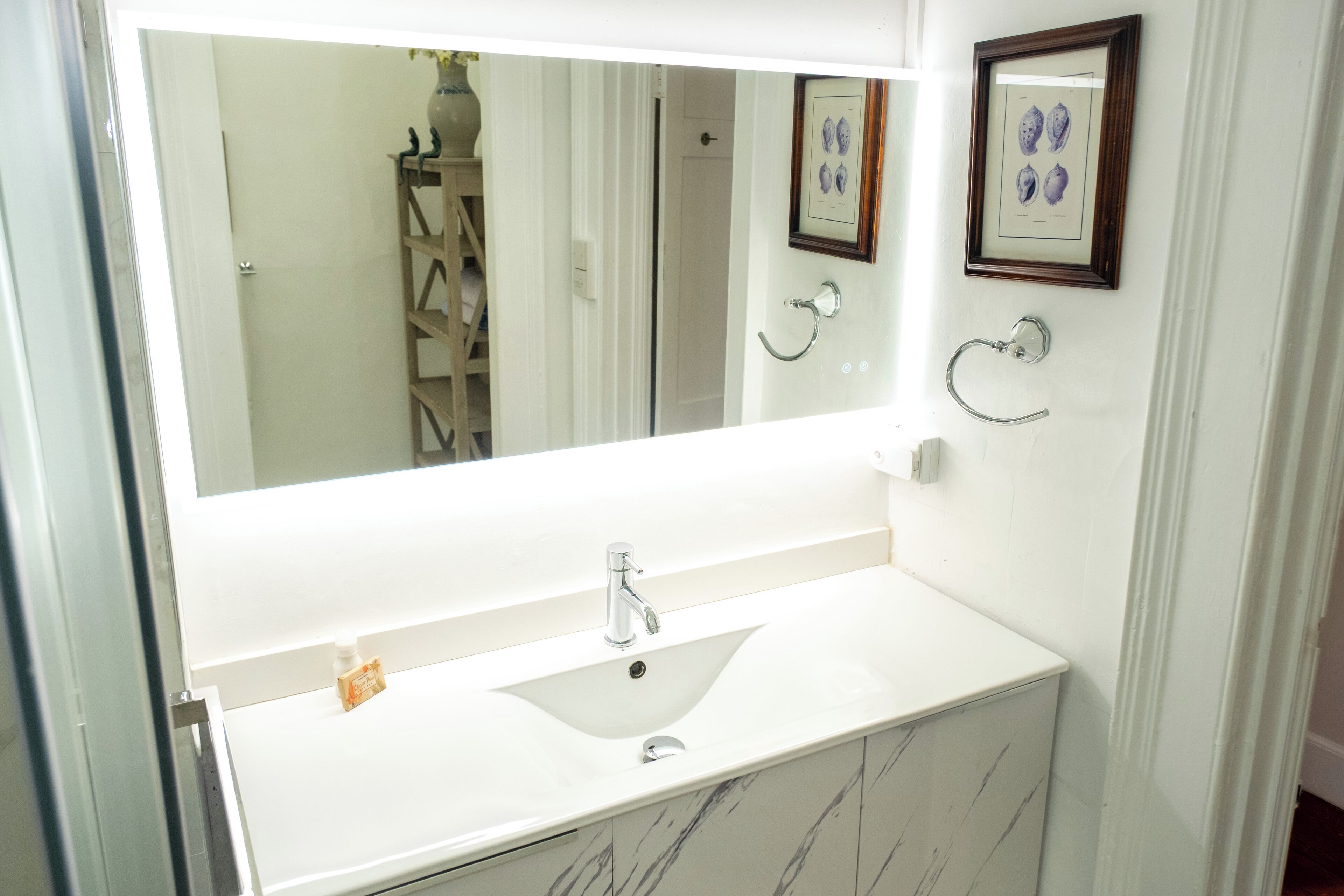 A bathroom with a white sink, a large mirror, and a framed picture on the wall.