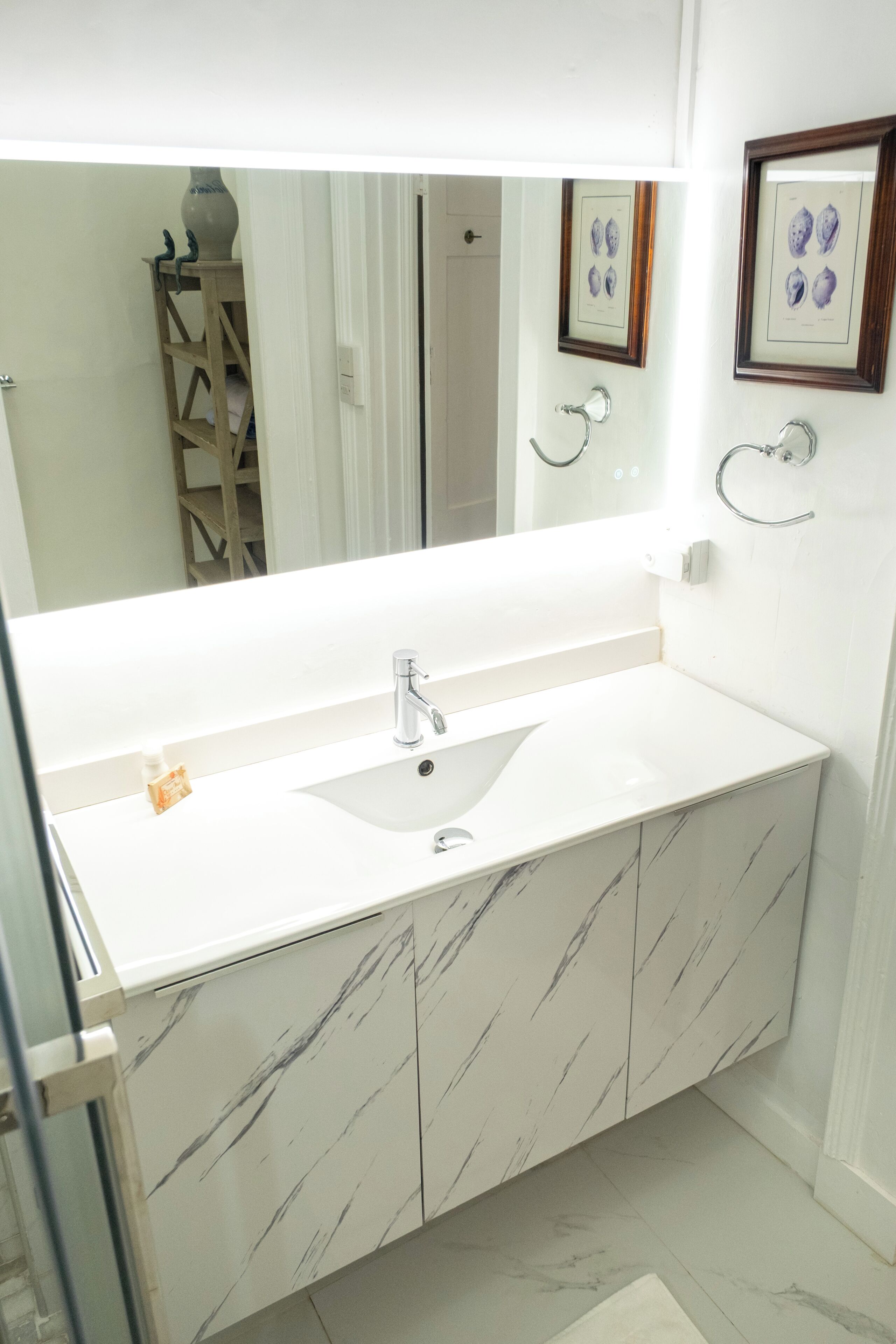 A bathroom with a white marble sink, a large mirror, and framed artwork on the wall.