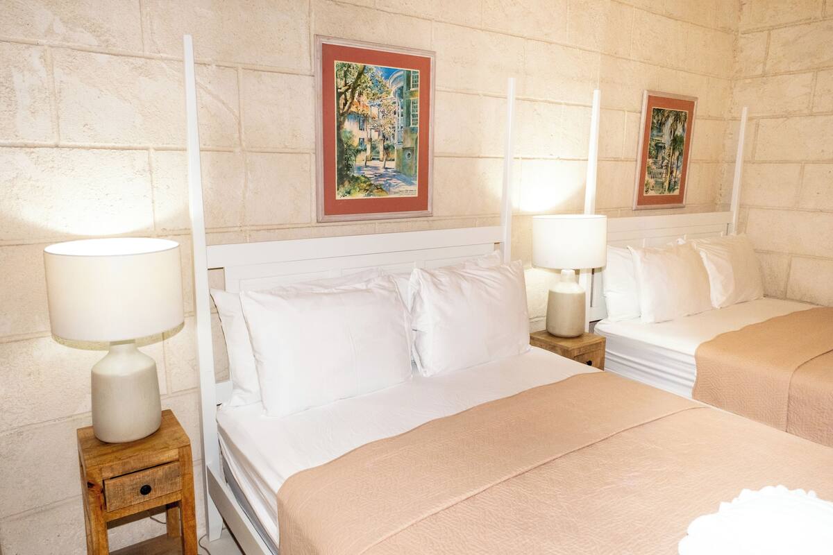 A hotel room with two beds, each with a white headboard and a bedside table with a lamp. There are framed pictures on the wall above each bed.