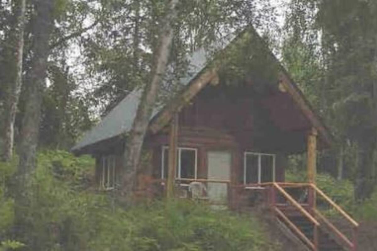 Une cabane rustique avec un toit à forte pente, un porche à l’avant et une petite terrasse.