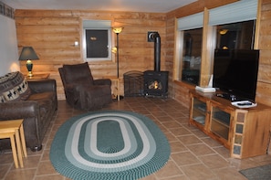 Interior de una cabaña de troncos con chimenea, un sofá, un televisor y una lámpara.