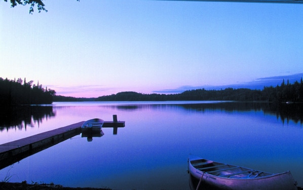Un lago tranquilo al anochecer con un muelle y una canoa.