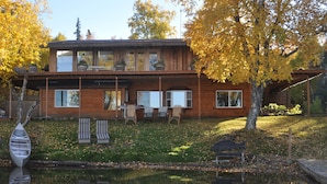 Puuinen mökki, jossa on terassi, ulkotila istumiseen ja lampi sen edessä.