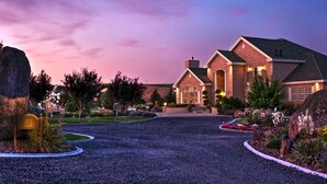 Une grande maison en briques avec une allée, entourée de jardins aménagés et d’une pelouse bien entretenue.