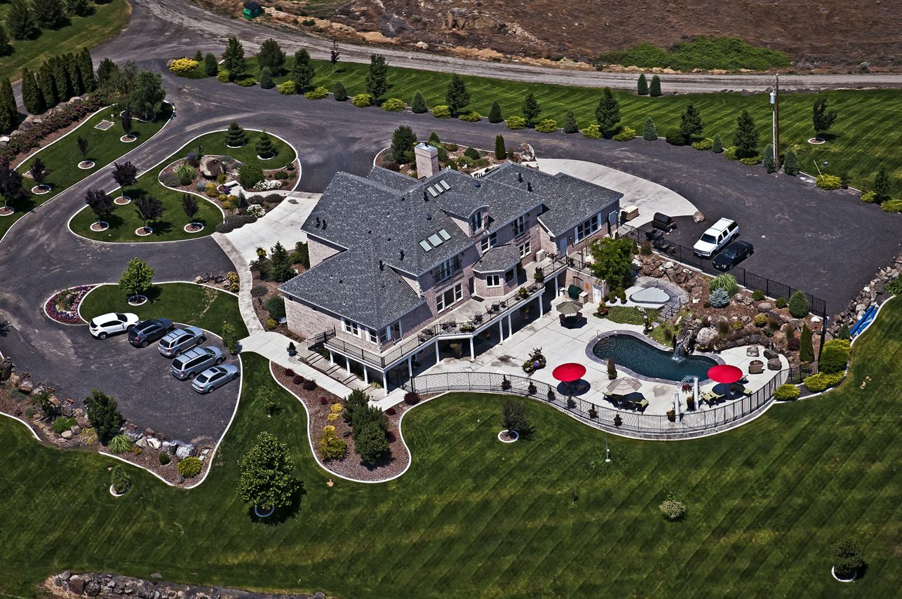 An aerial view of a large, modern house with a spacious driveway, a swimming pool, and a well-maintained lawn.