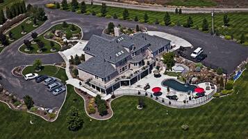An aerial view of a large, modern house with a spacious driveway, a swimming pool, and a well-maintained lawn.