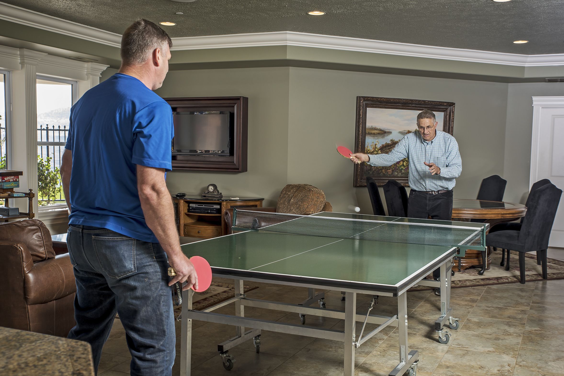 A ping pong table in a room with a large window, a framed painting, and a television.