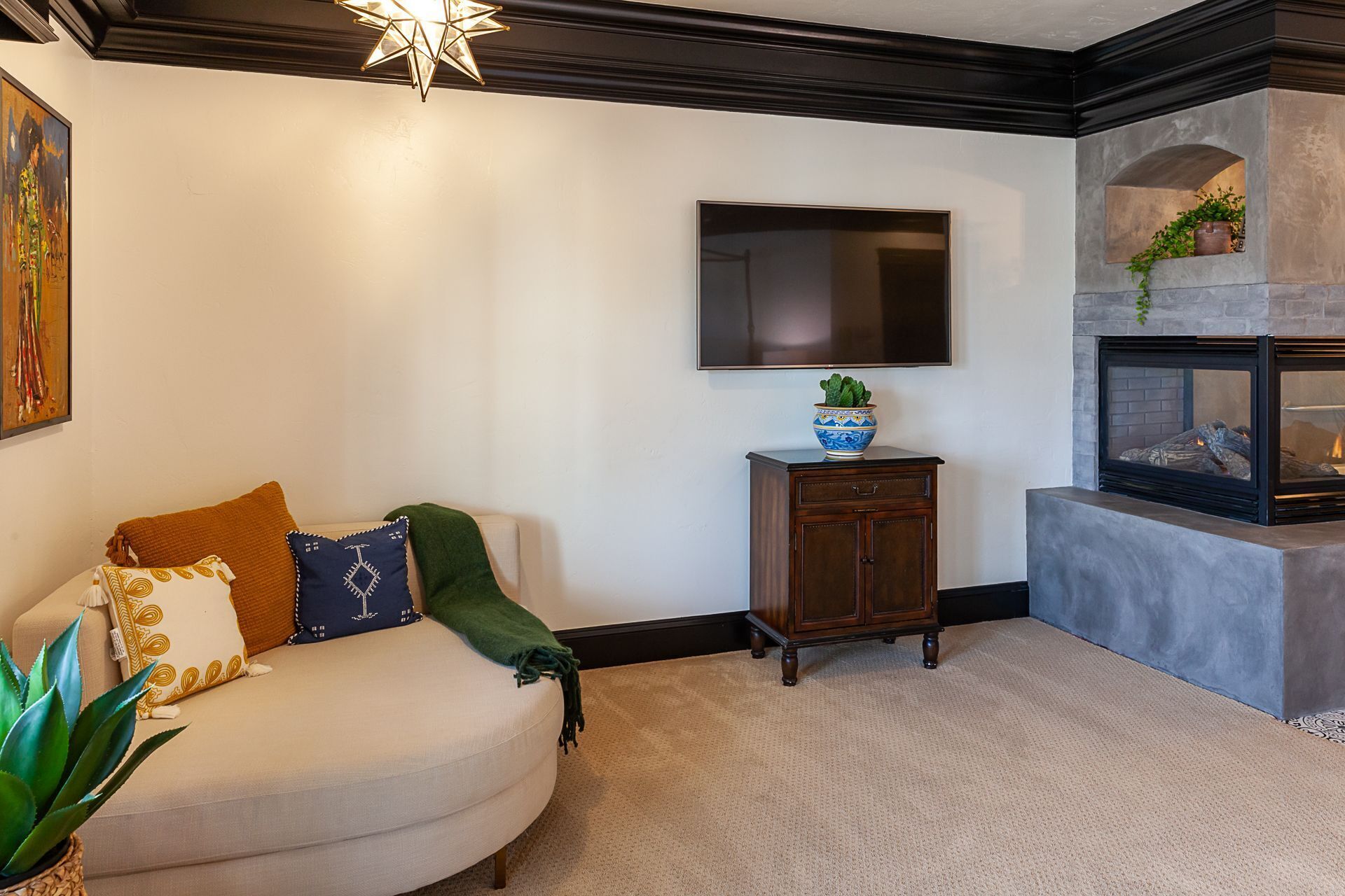 A living room with a sofa, a flat-screen TV, a fireplace, and a decorative bowl on a cabinet.