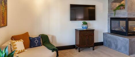A living room with a sofa, a flat-screen TV, a fireplace, and a decorative bowl on a cabinet.