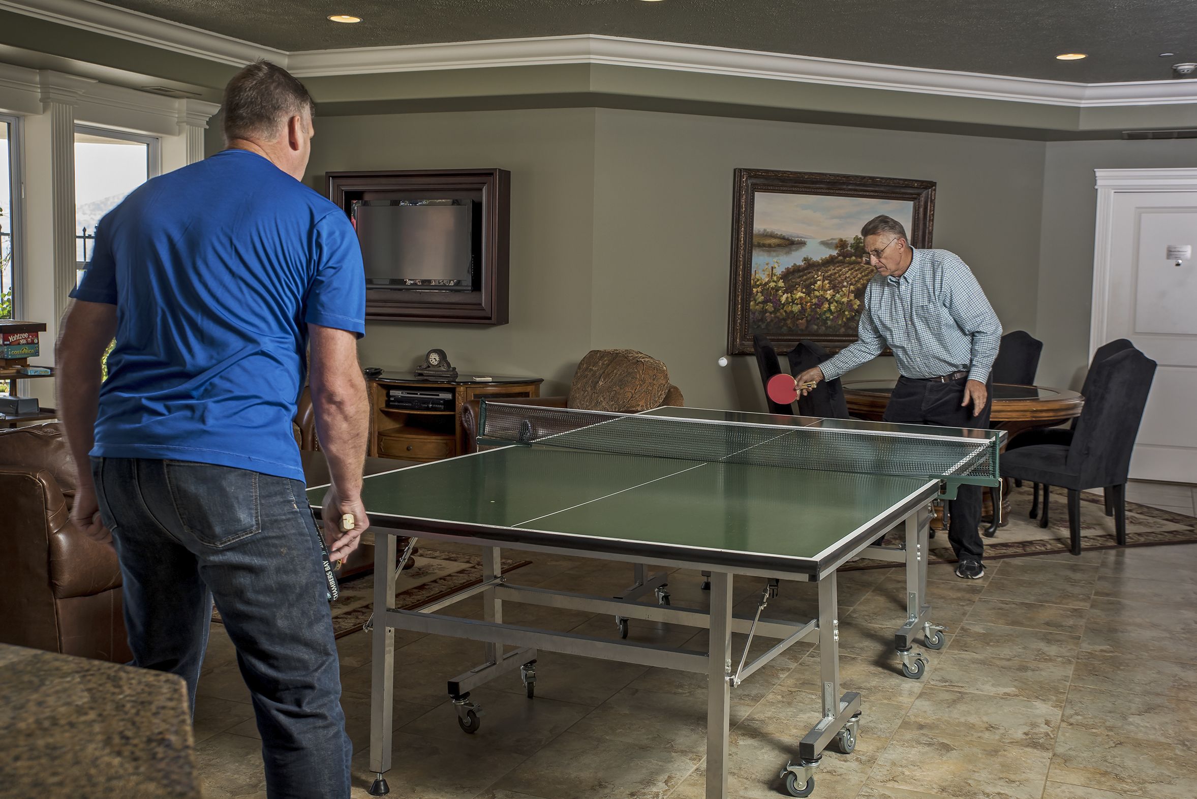 A ping pong table in a room with a large window, a painting on the wall, and a door.