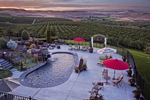 Un patio ajardinado con jacuzzi, mobiliario y vistas a viñedos.