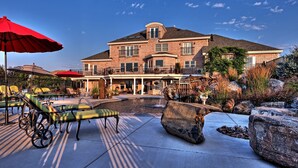 Une grande maison en briques dotée d’un patio aménagé avec des chaises longues et des parasols.
