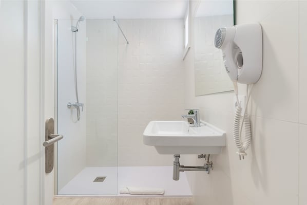 Un baño moderno con ducha de vidrio, lavamanos blanco y secador de pelo montado en la pared.