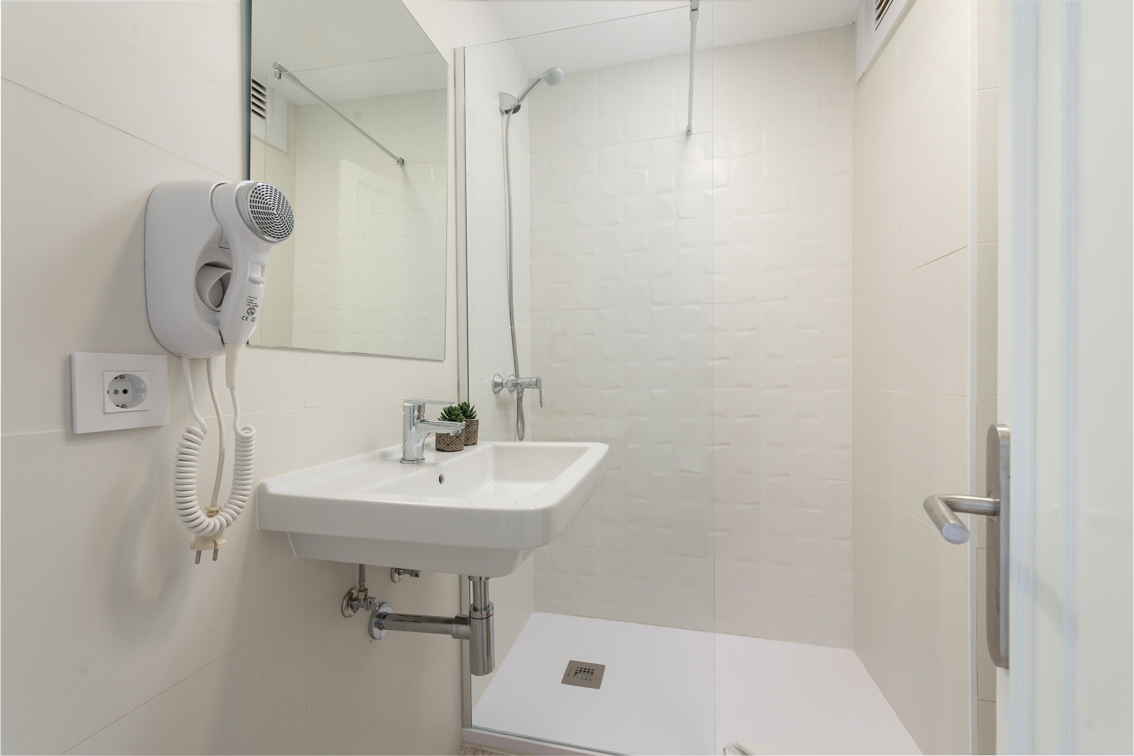 Une salle de bain moderne avec un lavabo blanc, un sèche-cheveux et une douche.